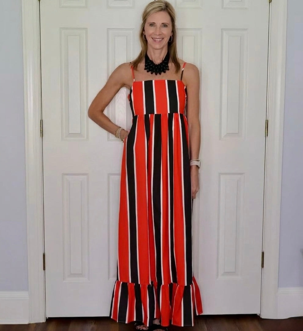 A woman modeling a sleeveless maxi dress with vertical red, black, and white stripes, standing in front of white paneled doors.