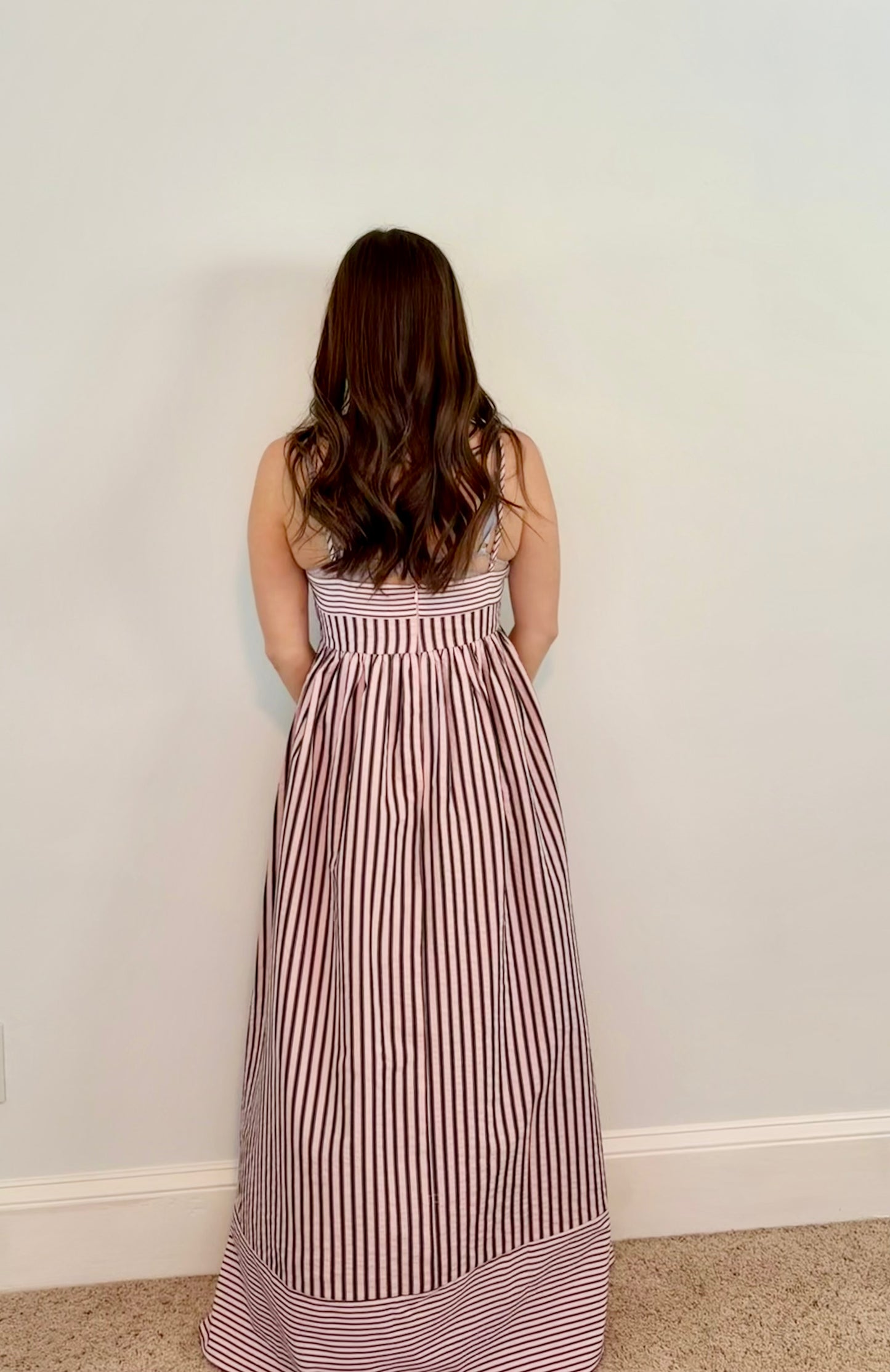Woman wearing a striped dress against a plain wall.