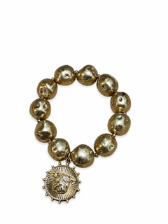 A gold-toned beaded bracelet with a circular medallion charm featuring a sunburst design and bulldogl face motif, shown on a plain white background.