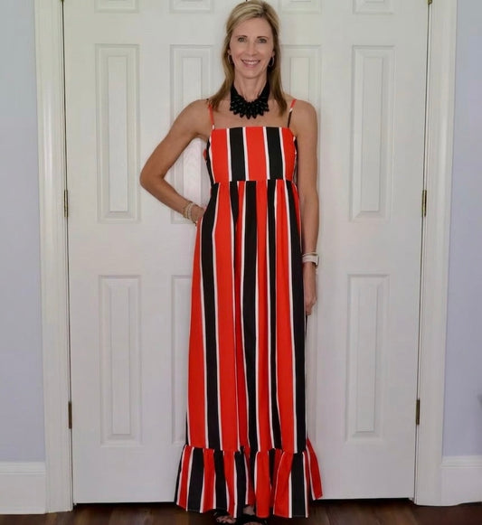 A woman modeling a sleeveless maxi dress with vertical red, black, and white stripes, standing in front of white paneled doors.