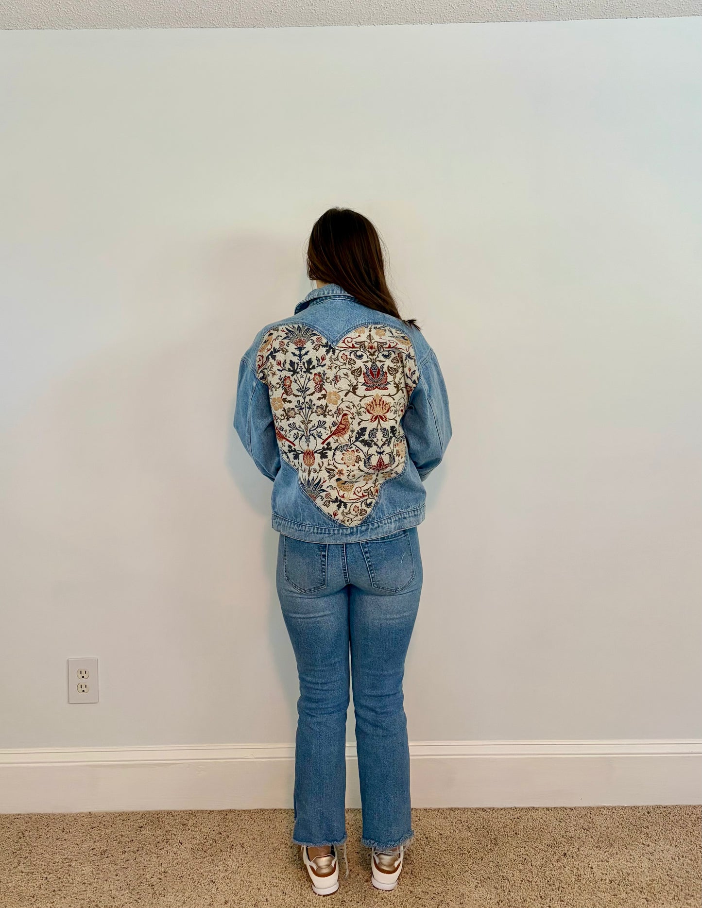 Person wearing a floral-patterned denim jacket against a plain wall.
