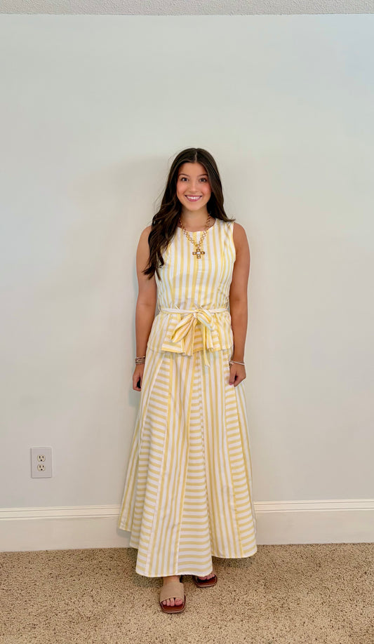 Woman wearing a yellow and white striped skirt set against a plain wall.