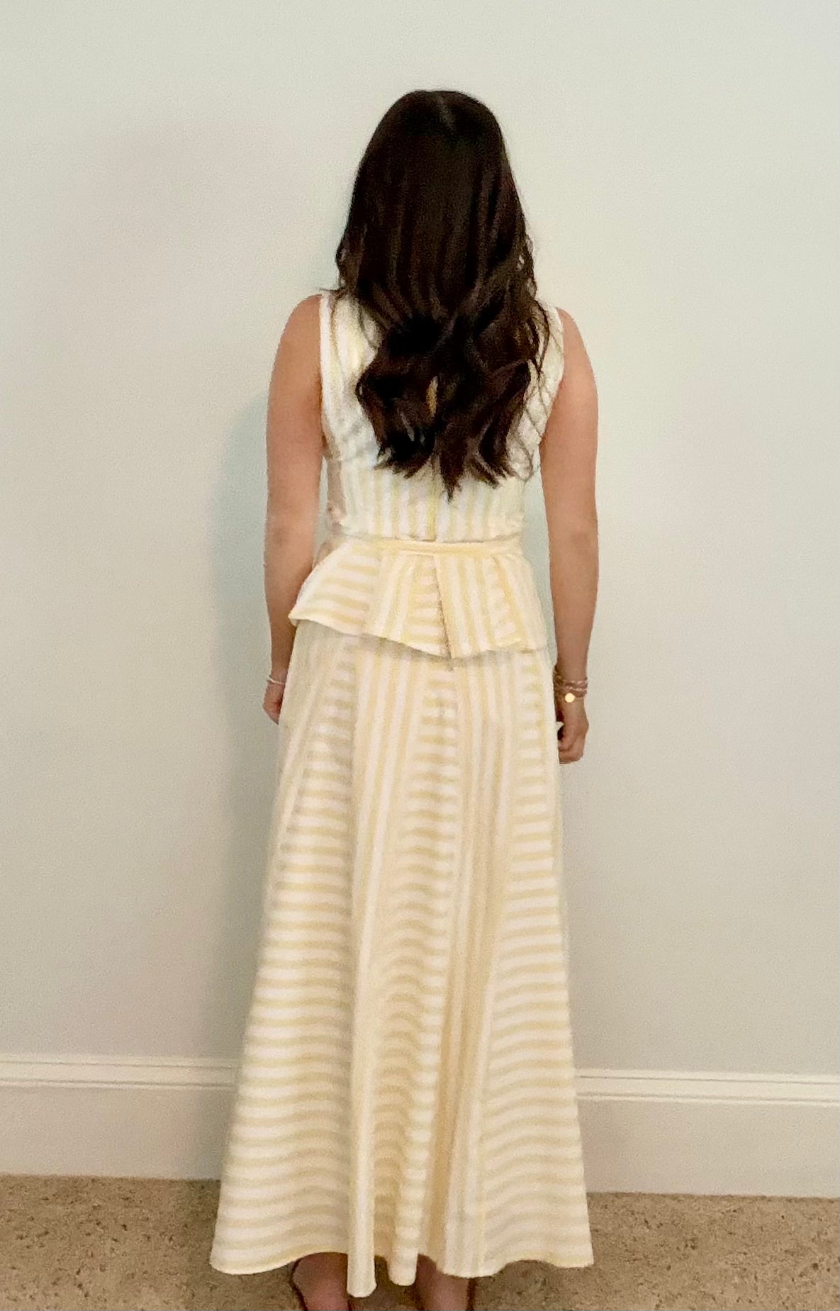 Woman wearing a yellow and white striped skirt set against a plain wall