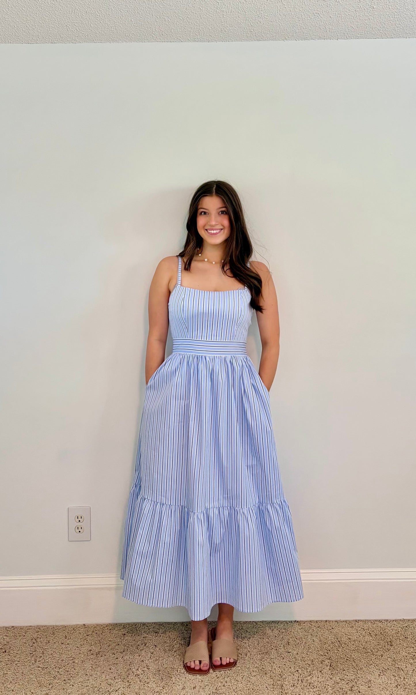 Woman wearing a blue striped dress against a plain wall.