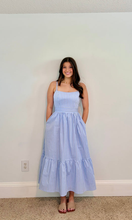 Woman wearing a blue striped dress against a plain wall.