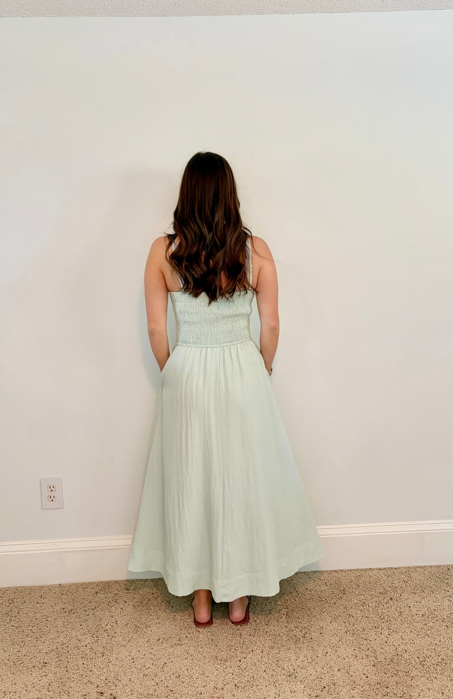 Woman wearing a light green dress standing against a white wall.