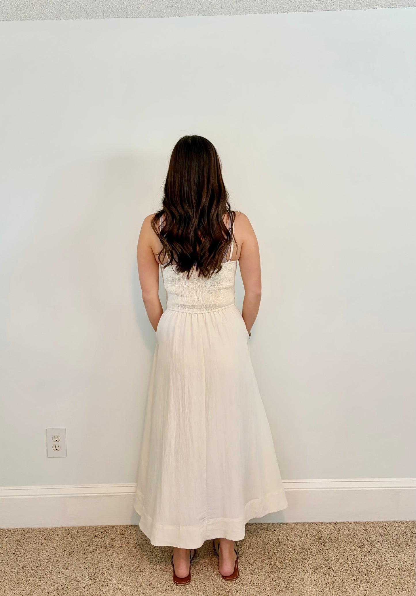 Woman wearing an ivory dress standing against a plain white wall.