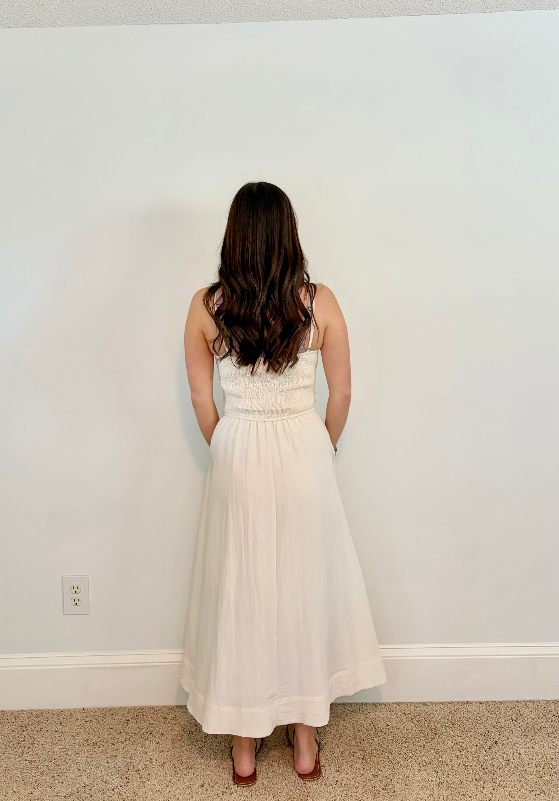 Woman wearing an ivory dress standing against a plain white wall.