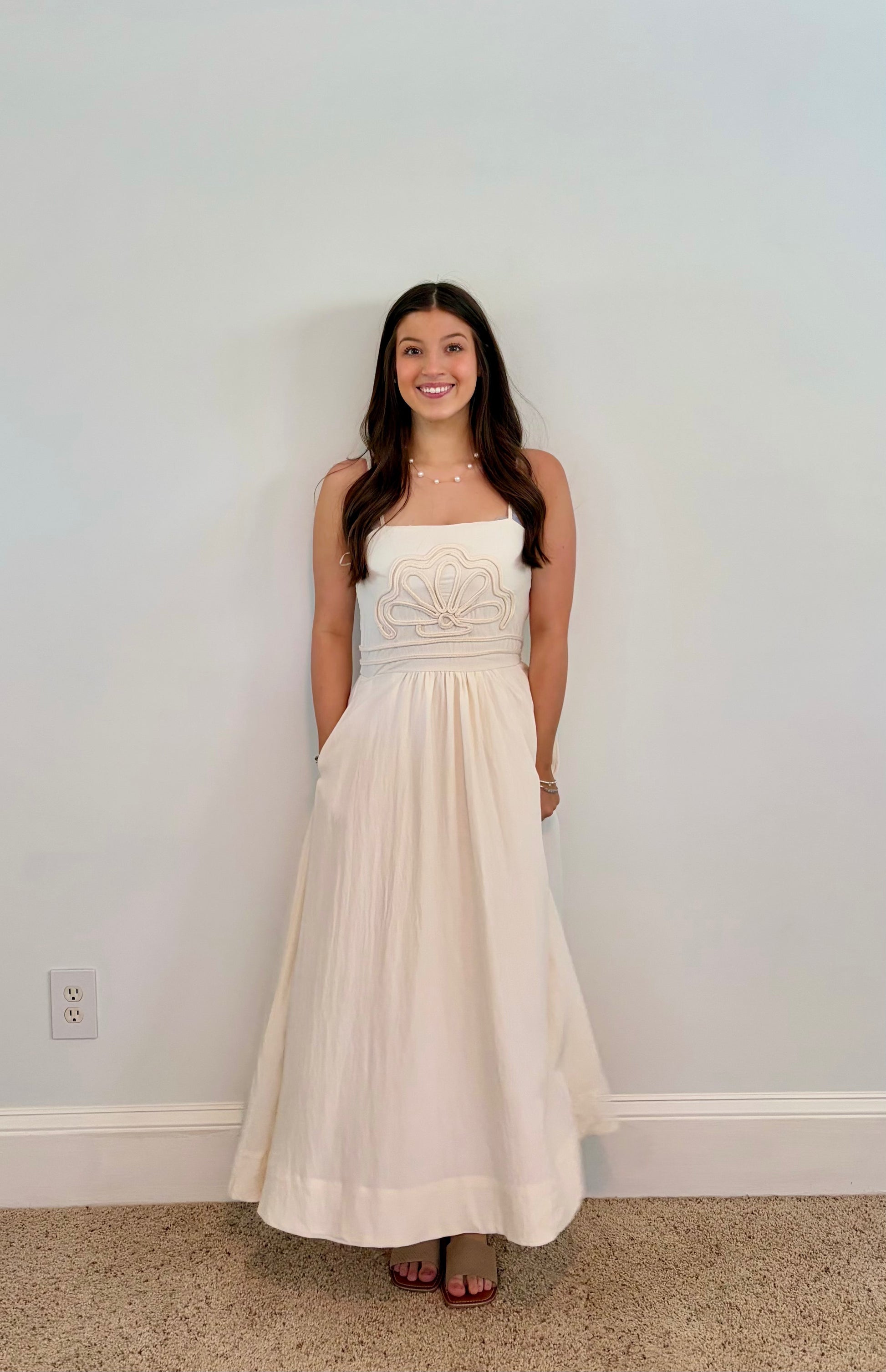 Woman wearing an ivory dress with shell applique standing against a plain wall.