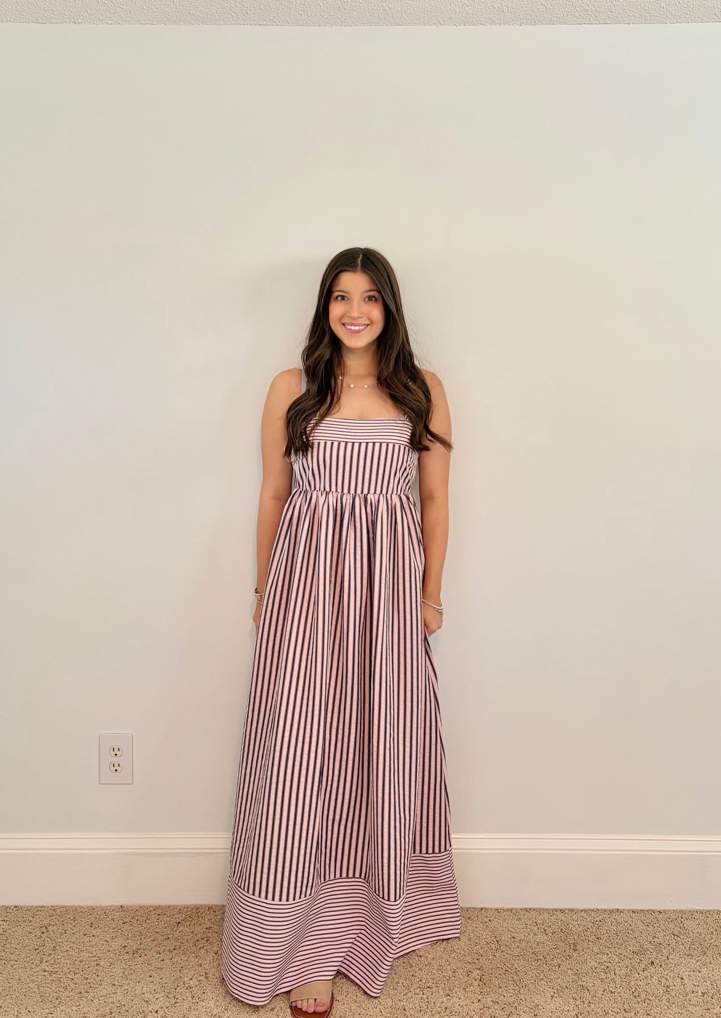 Woman wearing a striped dress standing against a plain wall.