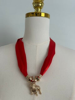 A red ribbon necklace with a gold bulldog pendant displayed on a cream-colored mannequin torso.